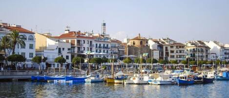 A marina with boats docked, surrounded by multi-story buildings with balconies and a clear sky.