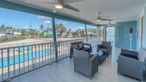 A covered outdoor area with wicker furniture, a pool, and a view of the beach and houses.