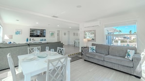 A modern living room with a dining area, grey sofas, a TV, and a large window with a view.