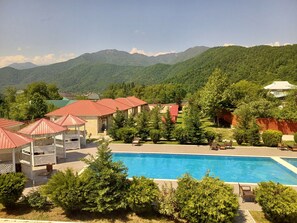 A hotel with a swimming pool, red-roofed buildings, and a mountainous backdrop. - Bliss Hotel (Gabala)
