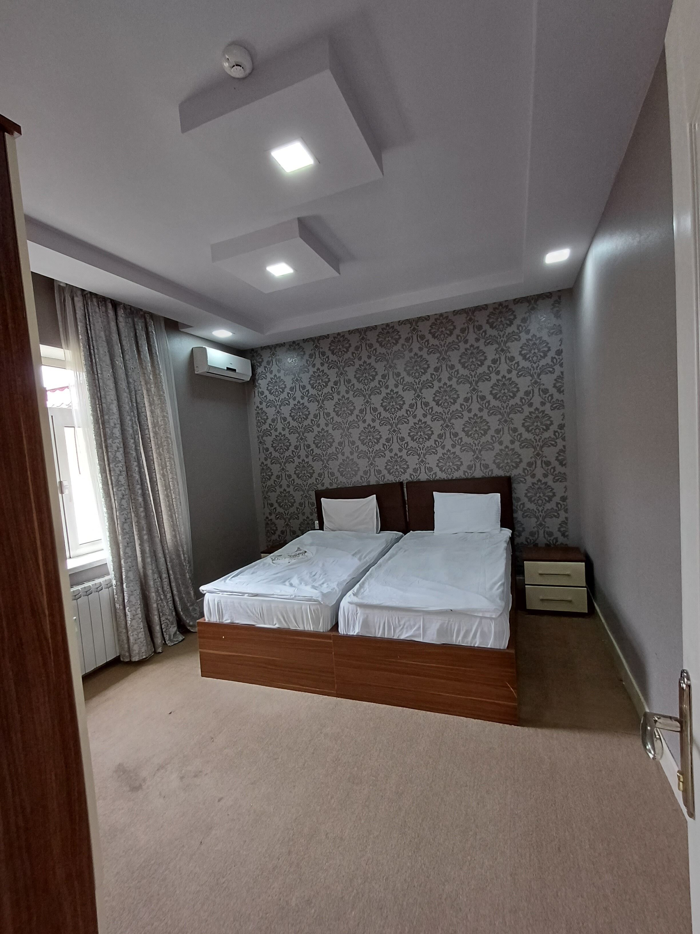 Une chambre à coucher avec un lit double, une table de chevet, un appareil de climatisation et une fenêtre avec des rideaux.