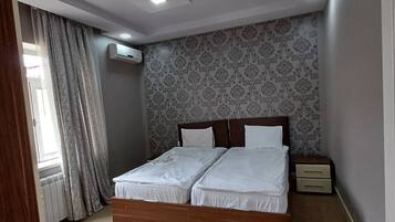 Une chambre à coucher avec un lit double, une table de chevet, un appareil de climatisation et une fenêtre avec des rideaux.