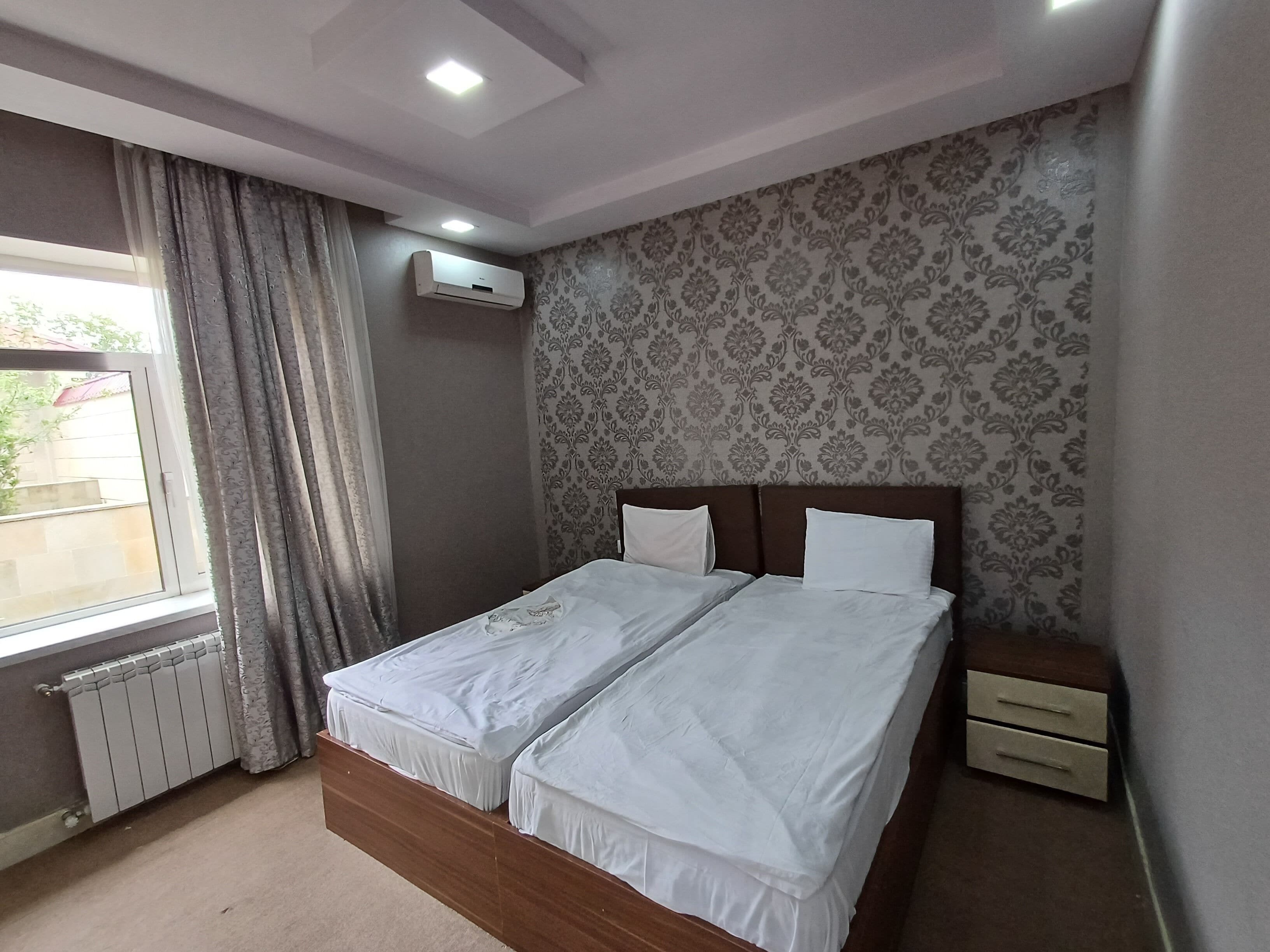 Une chambre avec un lit double, une table de chevet, une fenêtre avec des rideaux, un climatiseur et un radiateur.