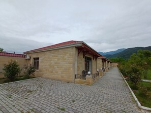 A building with a red roof and beige brick walls, a paved walkway, and a view of mountains in the background.