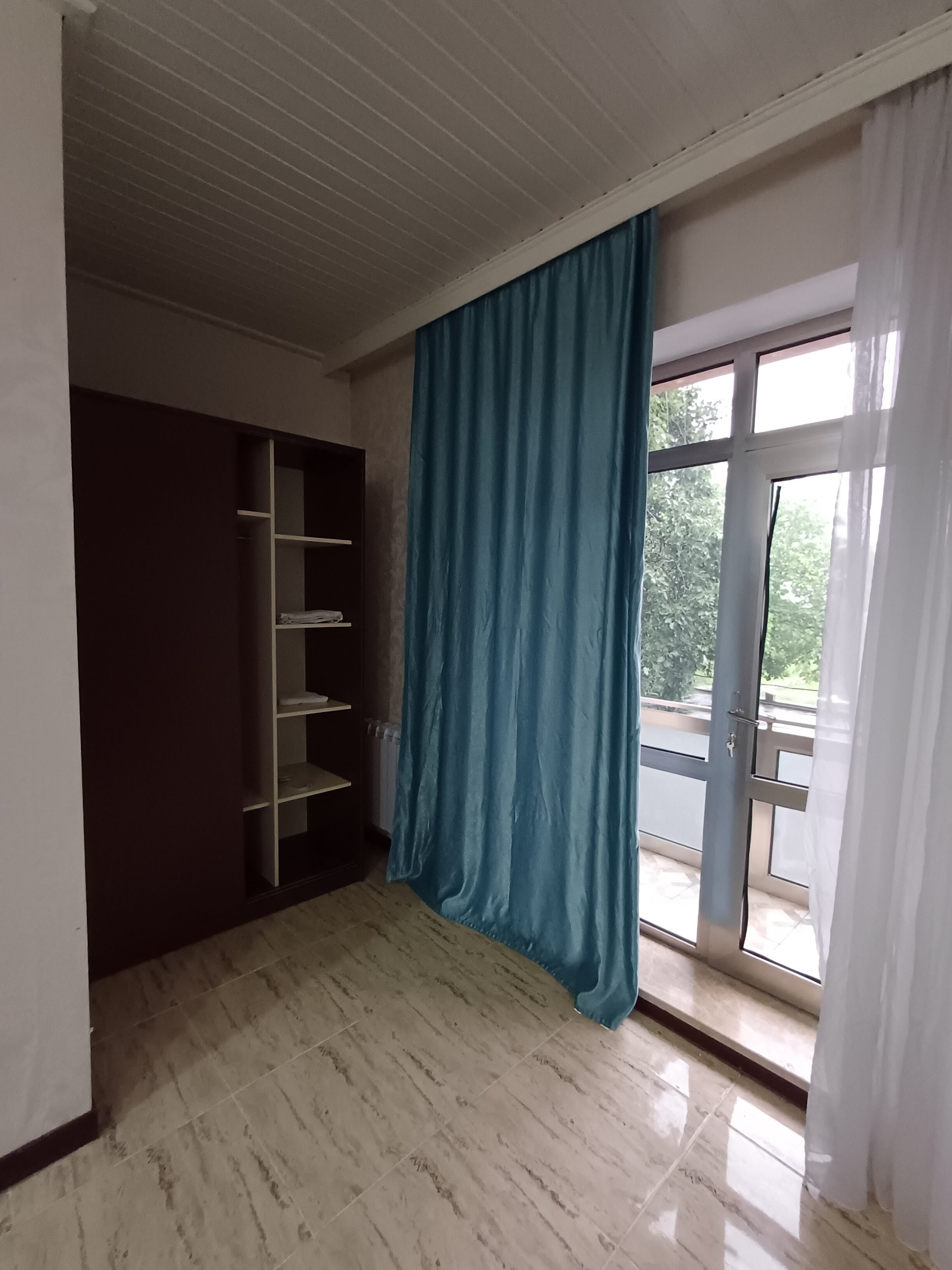 A room with a large window, a blue curtain, and a built-in wardrobe.