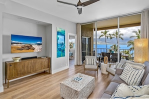 A modern living room with a large TV, wooden console, and a view of the ocean through large sliding doors.
