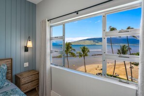 Ein Schlafzimmer mit großem Fenster und Meerblick, einer Nachttischlampe und einem Holznachttisch.