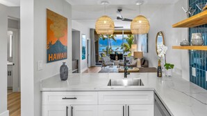 A modern kitchen with a large island, white cabinetry, and a view to the outdoors.
