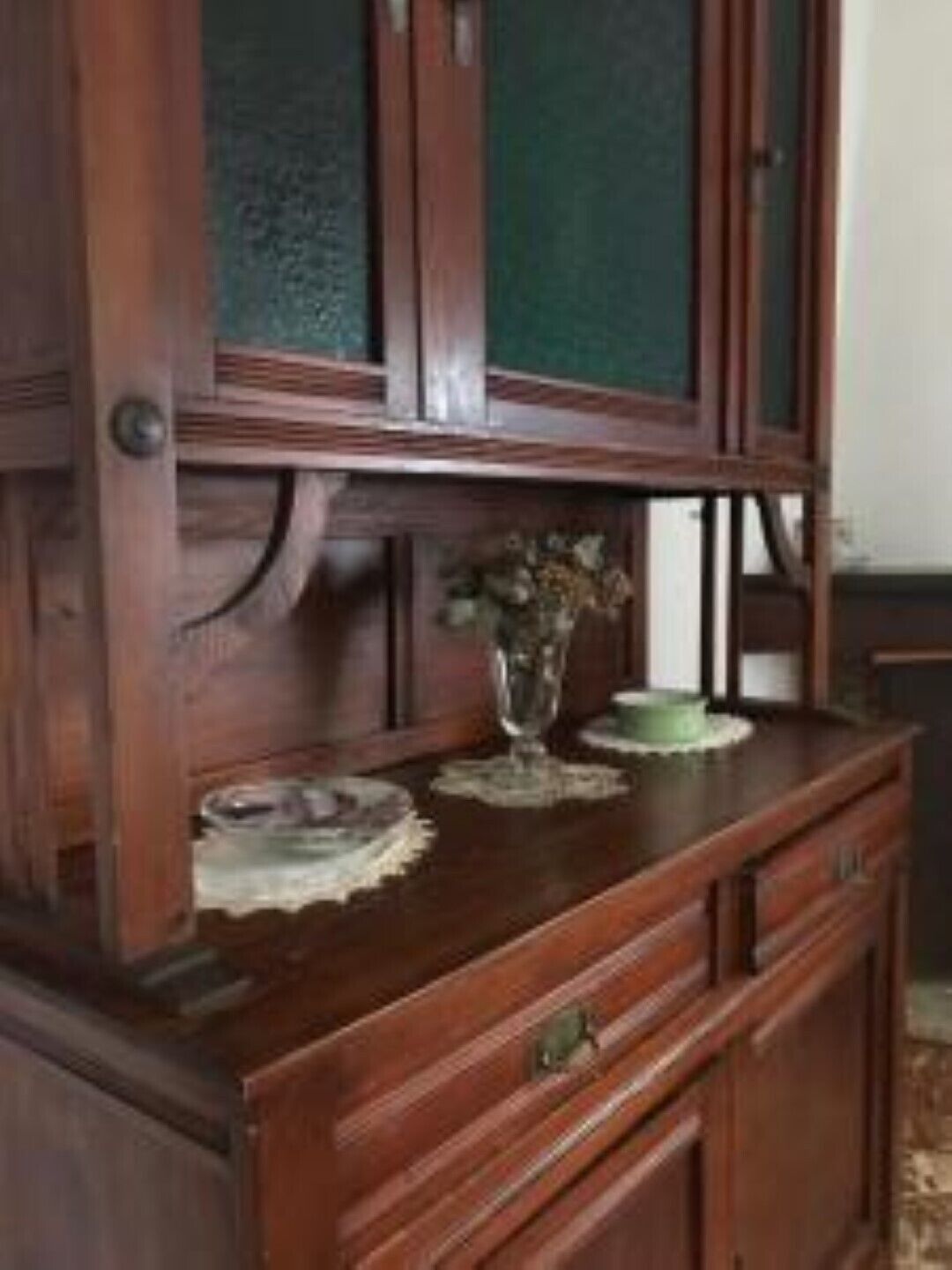 Un gabinete de madera con puertas de cristal, un jarrón con flores y un plato sobre la encimera.
