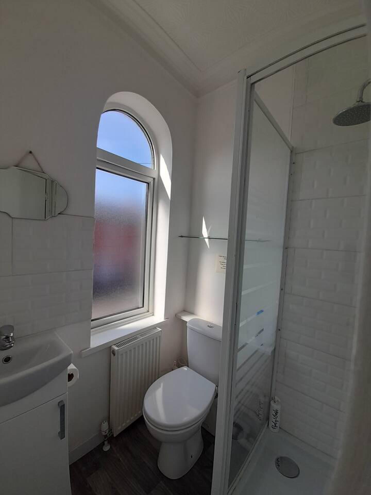 A compact bathroom with a white toilet, a window, a shower, and a radiator.