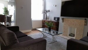 Een woonkamer met een bank, een glazen salontafel, een open haard en een televisie.
