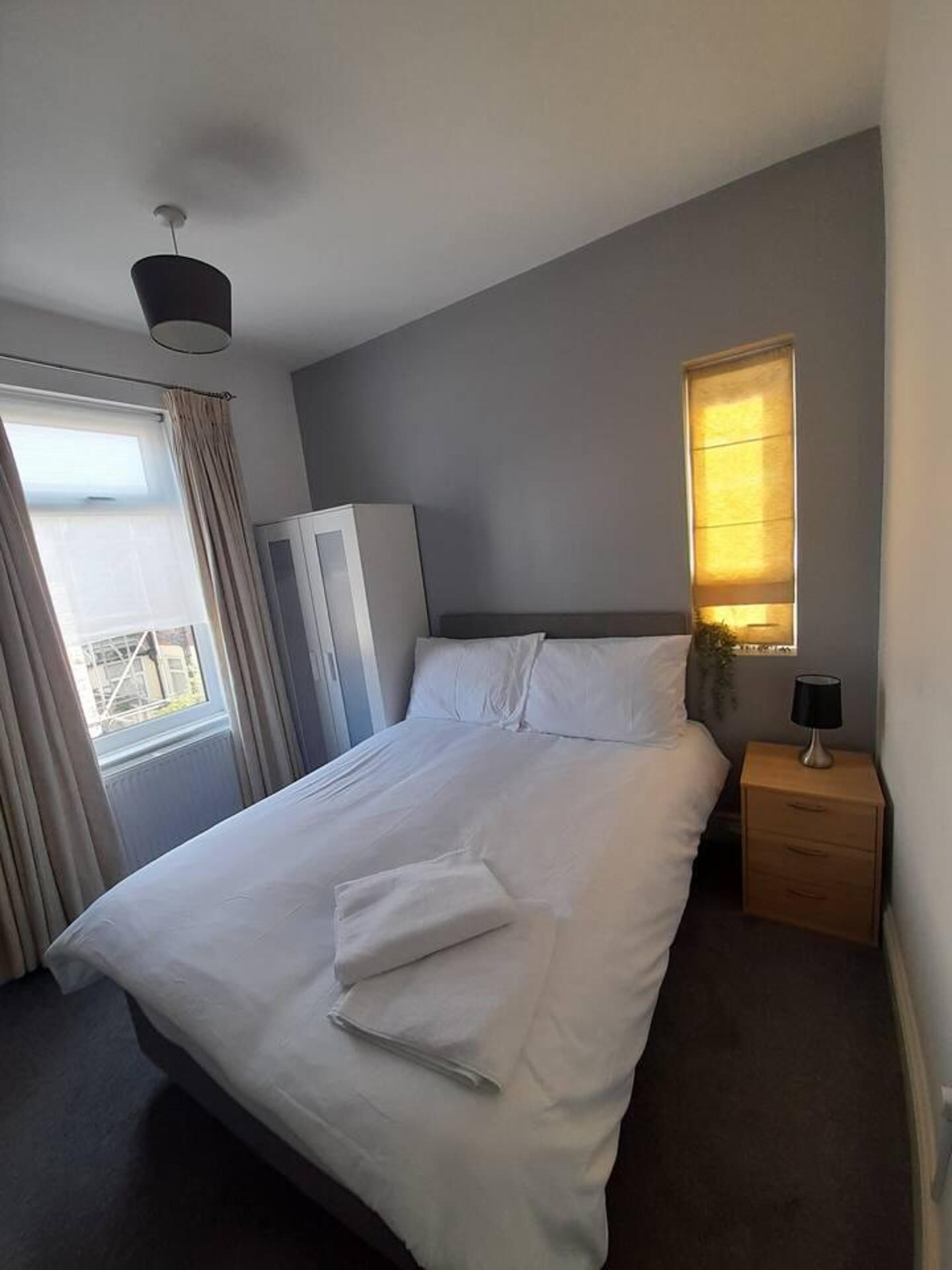 Un lit bien fait, avec du linge de lit blanc, une table de chevet avec une lampe et une fenêtre avec des rideaux.