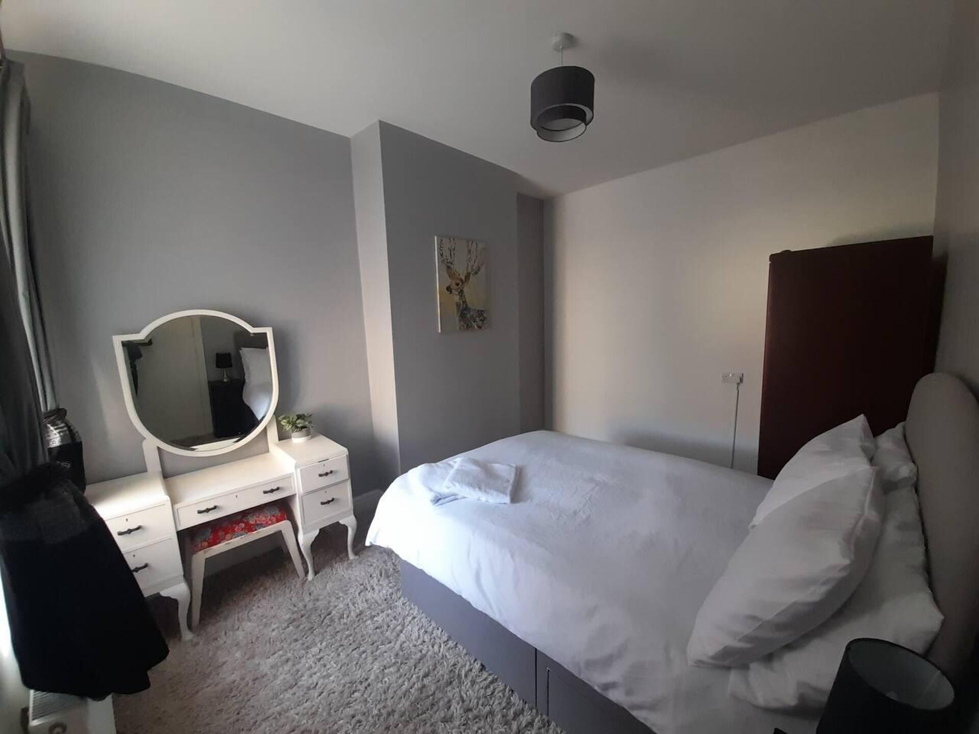Une chambre à coucher avec un lit, une commode avec un miroir, un tableau au mur et un luminaire au plafond.
