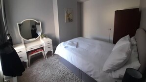 Een slaapkamer met een bed, een kaptafel met spiegel, een schilderij aan de muur en een plafondlamp.