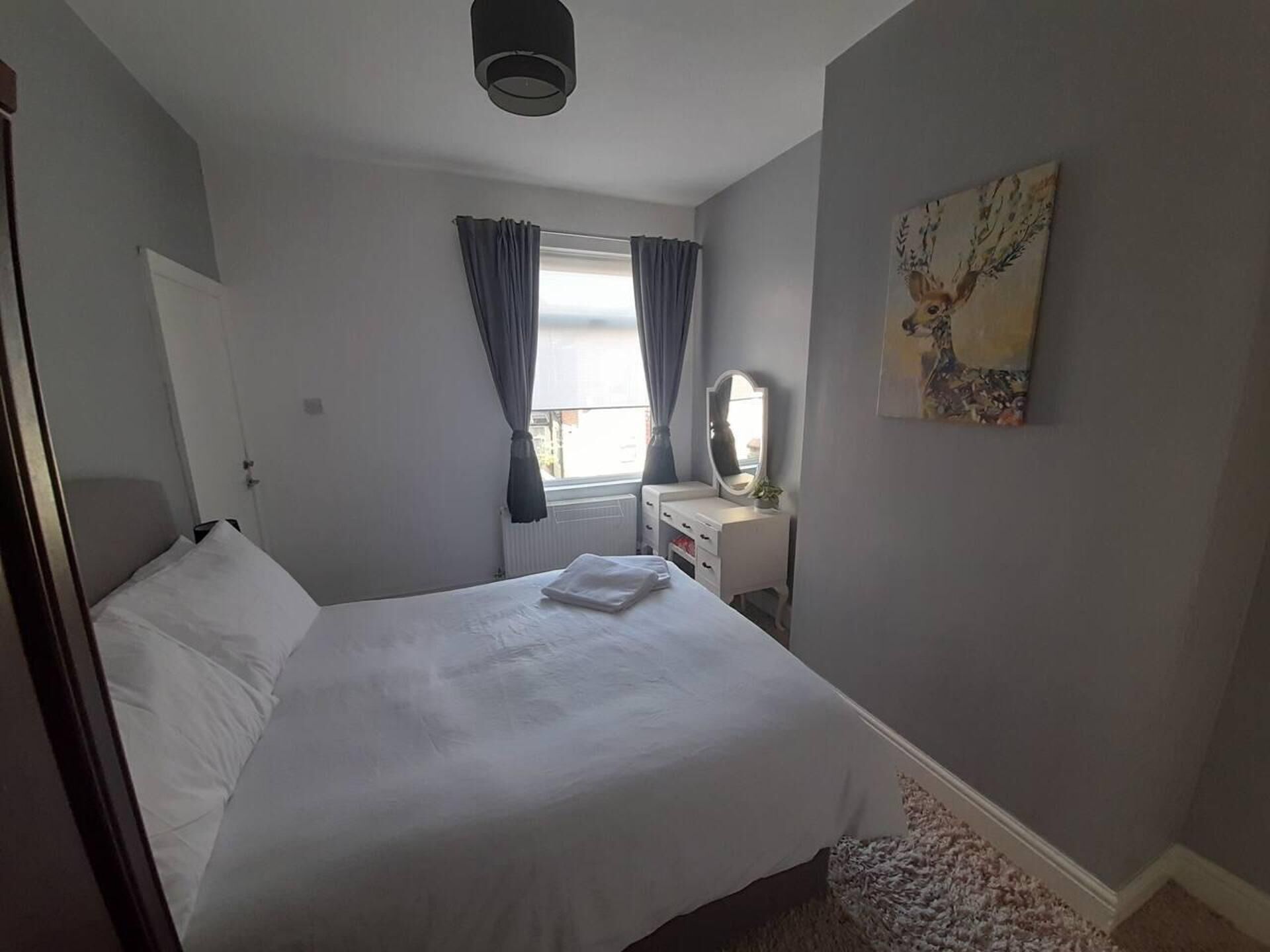 Une chambre à coucher avec un lit, une commode, un miroir et une fenêtre avec des rideaux.