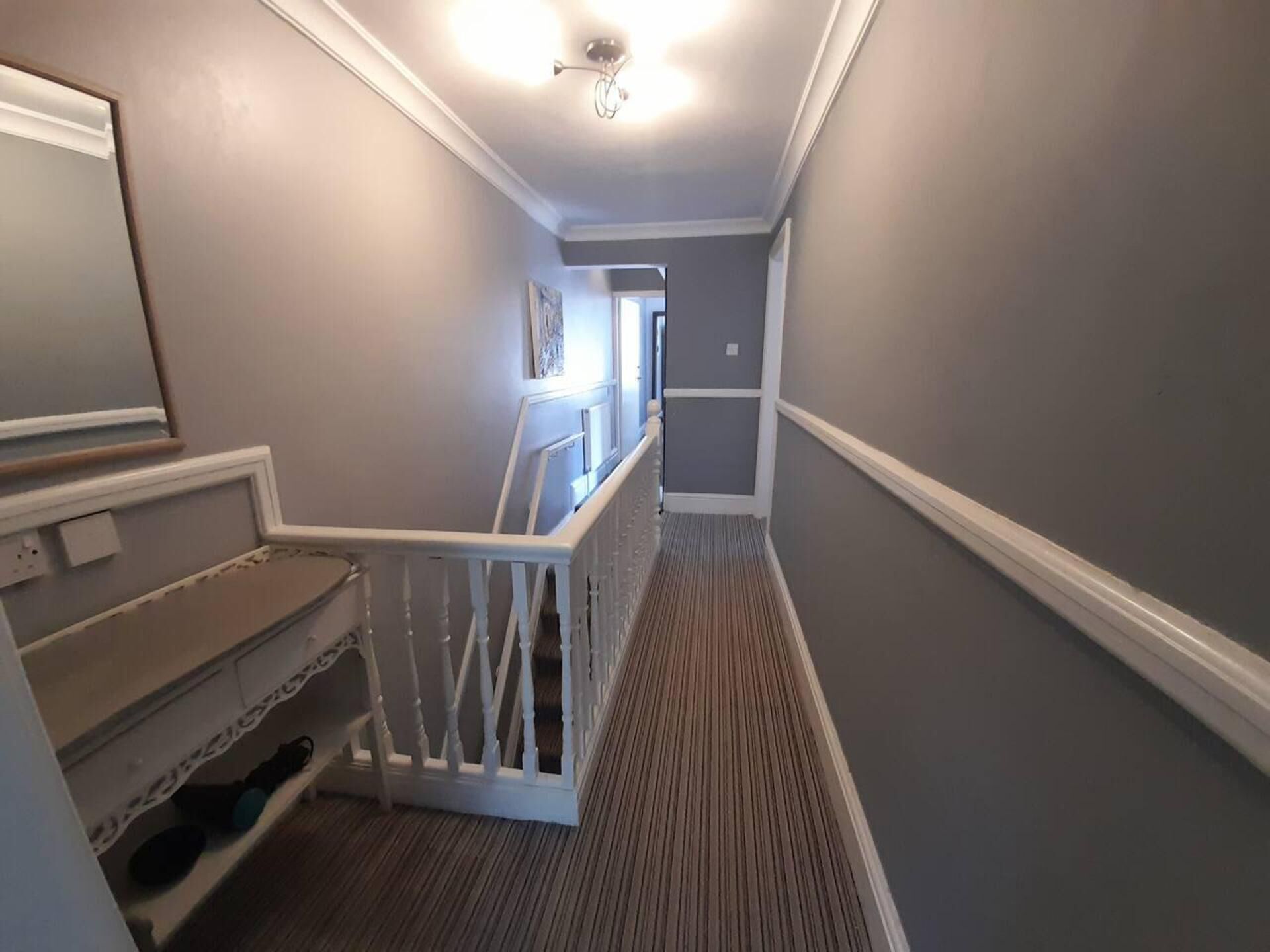 A narrow hallway with a white railing, a patterned carpet, and a ceiling light fixture.
