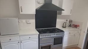 A kitchen with white cabinetry, a black range hood, a gas stove, and a built-in oven. There are two wall-mounted outlets and a coffee maker on the countertop. - Family, Long Stay, Contractors, Stags and Hens (Newcastle-upon-Tyne)