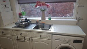 A compact kitchen with a built-in washing machine, a sink, and a window with a brick wall view. - Family, Long Stay, Contractors, Stags and Hens (Newcastle-upon-Tyne)