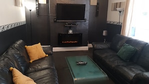 A living room with two black leather sofas, a green coffee table, a flat-screen TV mounted on the wall, and a fireplace below the TV. - Family, Long Stay, Contractors, Stags and Hens (Newcastle-upon-Tyne)