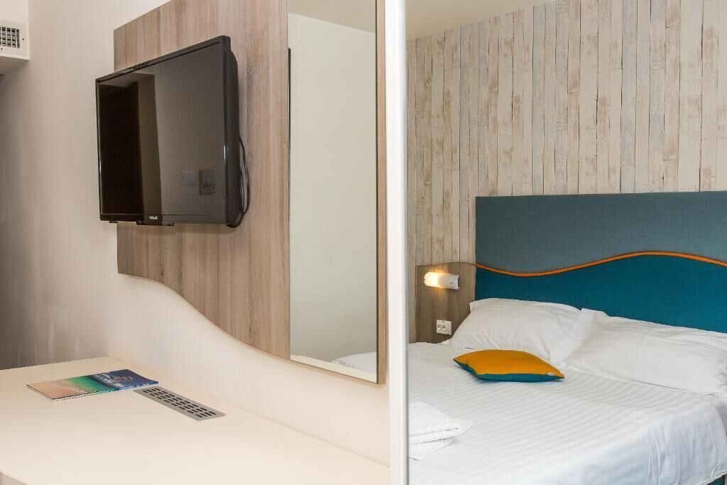 Una habitación de hotel con cama, mesita de noche, televisor en la pared y espejo.