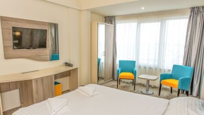 A hotel room with a large bed, a desk with a chair, a TV mounted on the wall, and a window with curtains. - HOTEL RIVIERA (Constanta)