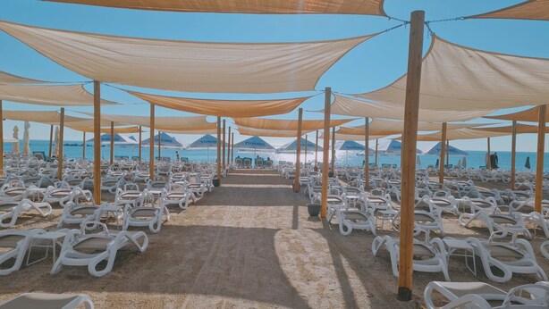 A beachside seating area with rows of white lounge chairs under large canopies, leading to a view of the sea. - HOTEL RIVIERA (Constanta)