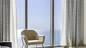 Une pièce avec une grande fenêtre, une chaise et un vase contenant des tiges de roseau.