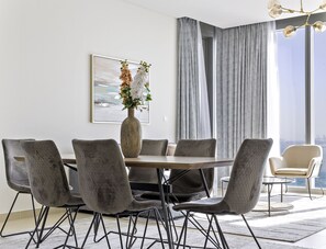 A modern dining room with a round table, grey upholstered chairs, and a vase with flowers. - WelHome - Spectacular 2BR Apartment with Panoramic Sea Views (Dubai)
