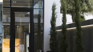 A modern building entrance with a glass door, potted plants, and a tiled floor. - Center Hotel (Sarandë)