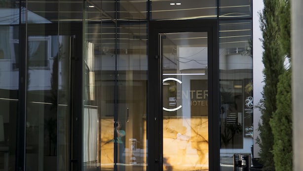 A modern hotel entrance with glass doors, a visible reception area, and a potted plant to the right. - Center Hotel (Sarandë)