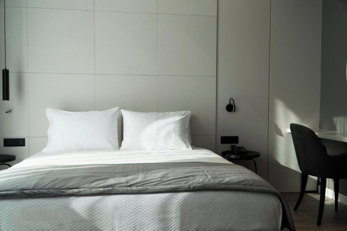 A modern hotel room with a large bed, a desk, and a chair.
