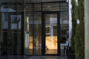 Entrada de un hotel con puerta de vidrio, mostrador de recepción y un interior visible con pared de mármol.