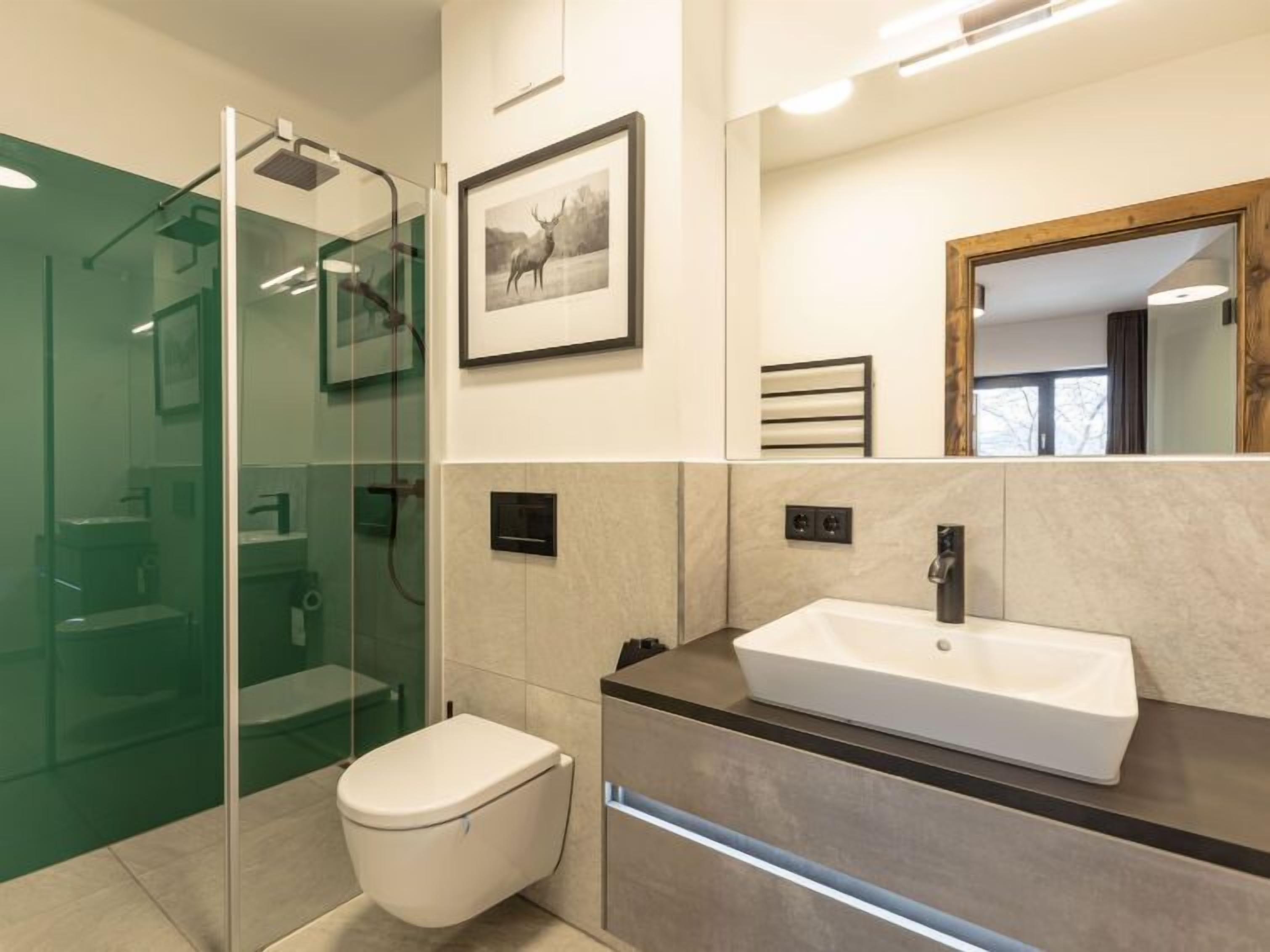 A modern bathroom with a glass shower enclosure, a white toilet, a sink with a mirror, and a framed picture on the wall.