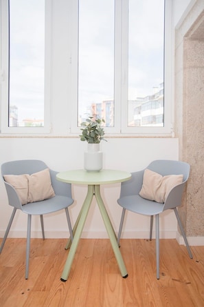 A room with two grey chairs, a small round table with a white vase, and a window with a view of buildings.
