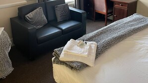 Een hotelkamer met een bed, een bureau, een stoel, een bank en een raam met gordijnen.