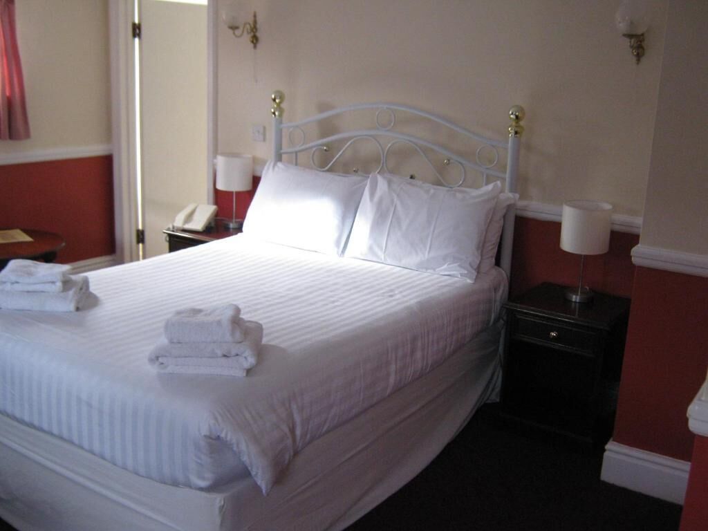 A neatly made bed with white linens and pillows, a bedside table with a lamp, and a telephone.