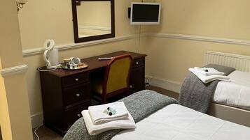 Una habitación de hotel con cama, escritorio con silla, espejo, televisión y un cuadro en la pared.