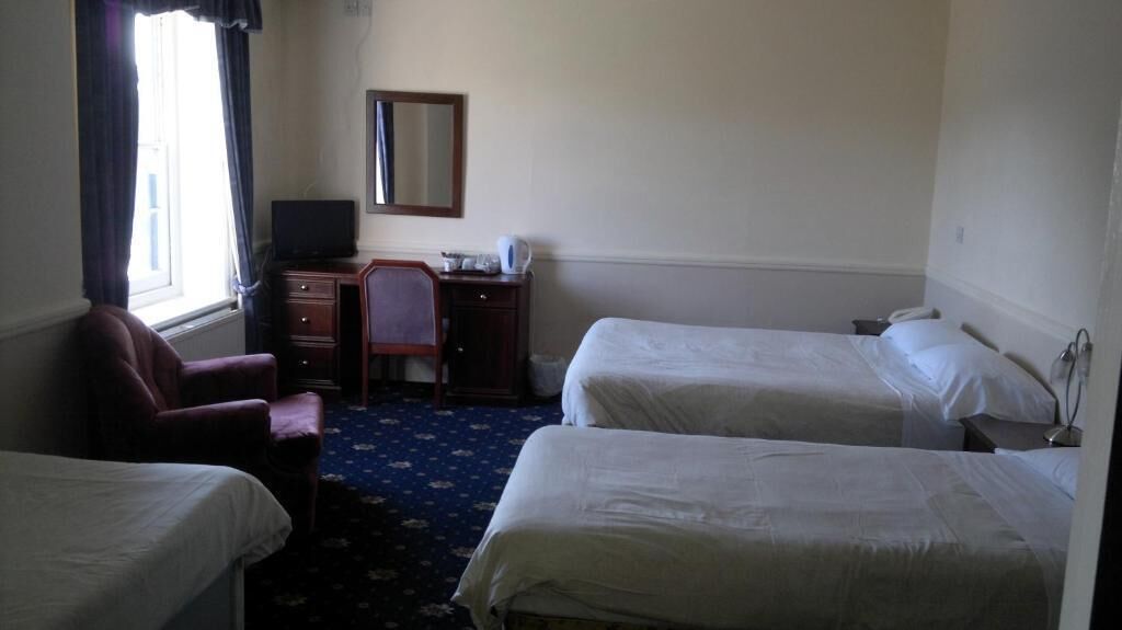 Habitación de hotel con dos camas individuales, un escritorio con silla, televisión y un espejo en la pared.