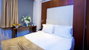 A hotel room with a bed, a bedside table with a bowl of fruit and a vase of flowers, and a window with curtains. - THE COACH HOTEL (Istanbul)