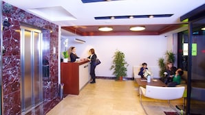 A hotel lobby with a reception desk, a seating area with a table and chairs, and a reception area with a plant and a sign that reads "COACH". - THE COACH HOTEL (Istanbul)