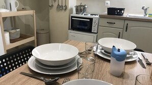 Une cuisine avec une table en bois mise pour le repas, un four à micro-ondes et divers ustensiles accrochés au mur.