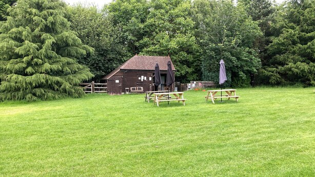 A rustic barn with picnic tables in a grassy field. - Woodlands Basic Bell Tent (Grantham)
