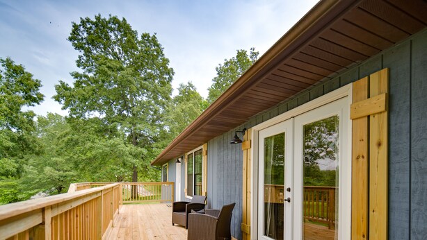A wooden deck with a railing, a covered seating area with chairs, and a glass door leading to an outdoor area. - Brand New Farmhouse Style Listing with views of the beautiful Spring River! (Mammoth Spring)