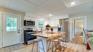 A modern kitchen with a central island, bar stools, a microwave, oven, refrigerator, and a potted plant. - Brand New Farmhouse Style Listing with views of the beautiful Spring River! (Mammoth Spring)