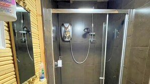 Cabina de ducha con paredes de vidrio, ducha de mano, grifo en la pared y dispensador de jabón.