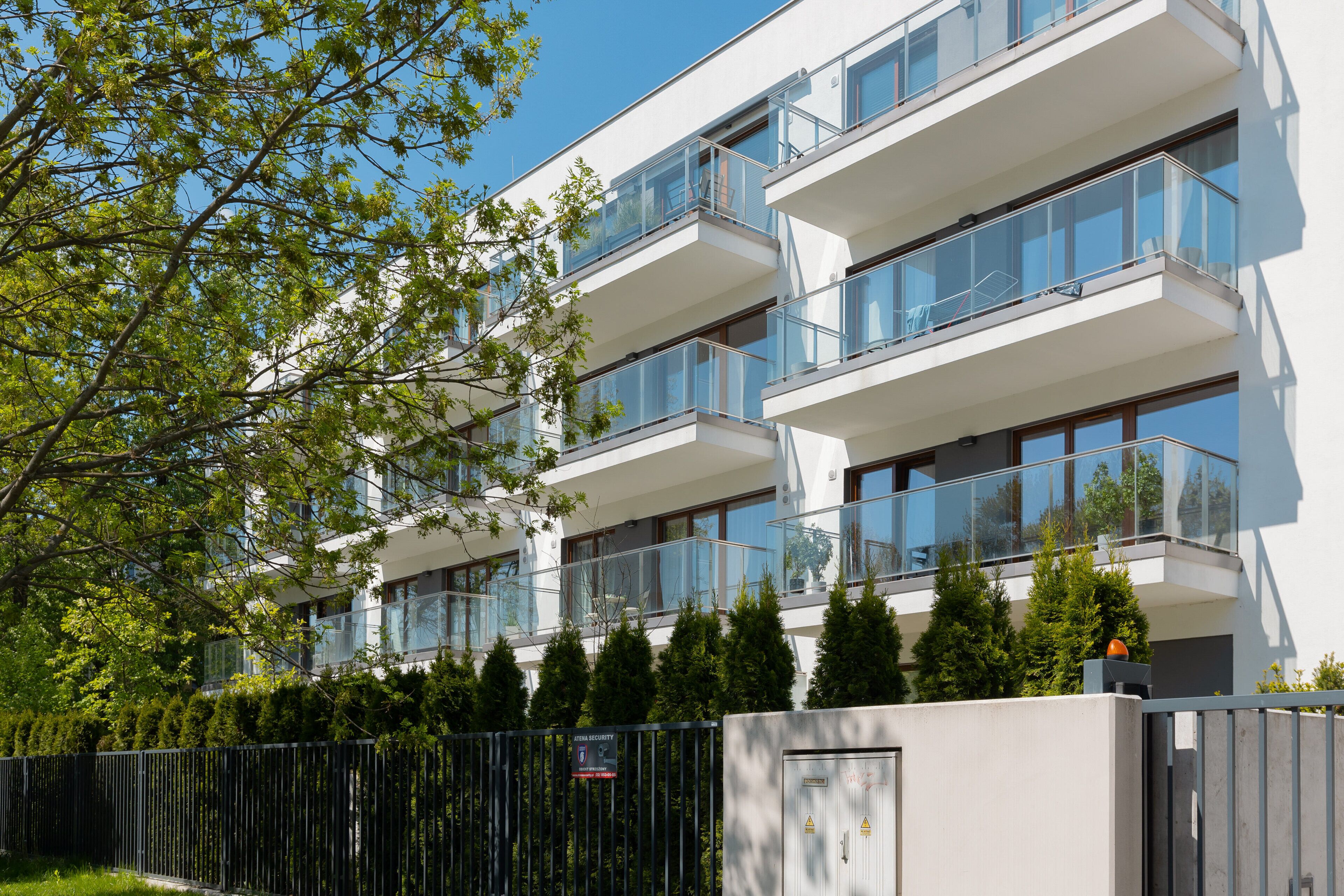 A multi-story residential building with balconies, a gated entrance, and a clear sky.