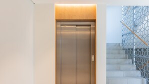 An elevator with a wooden panel above it and a staircase with a geometric metal railing to the right. - Boutiq Park Apartment Warsaw by Renters (Warsaw)