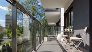 A modern balcony with glass railings, a seating area with a table and chairs, and a view of the surrounding greenery and buildings. - Boutiq Park Apartment Warsaw by Renters (Warsaw)