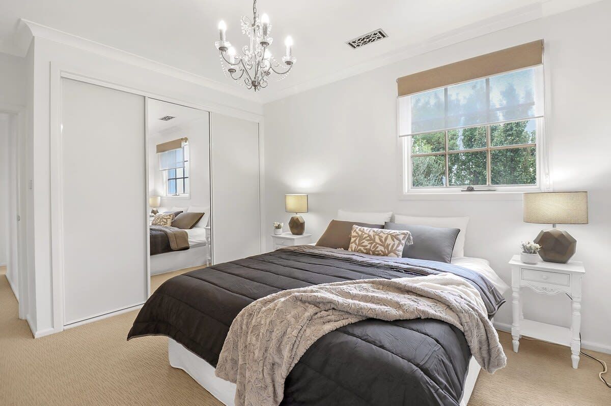 A bedroom with a large bed, a wardrobe, a window with a view, and a chandelier.