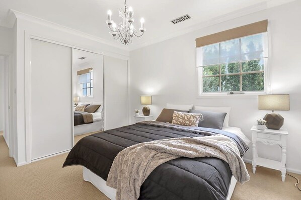 A bedroom with a large bed, a wardrobe, a window with a view, and a chandelier.